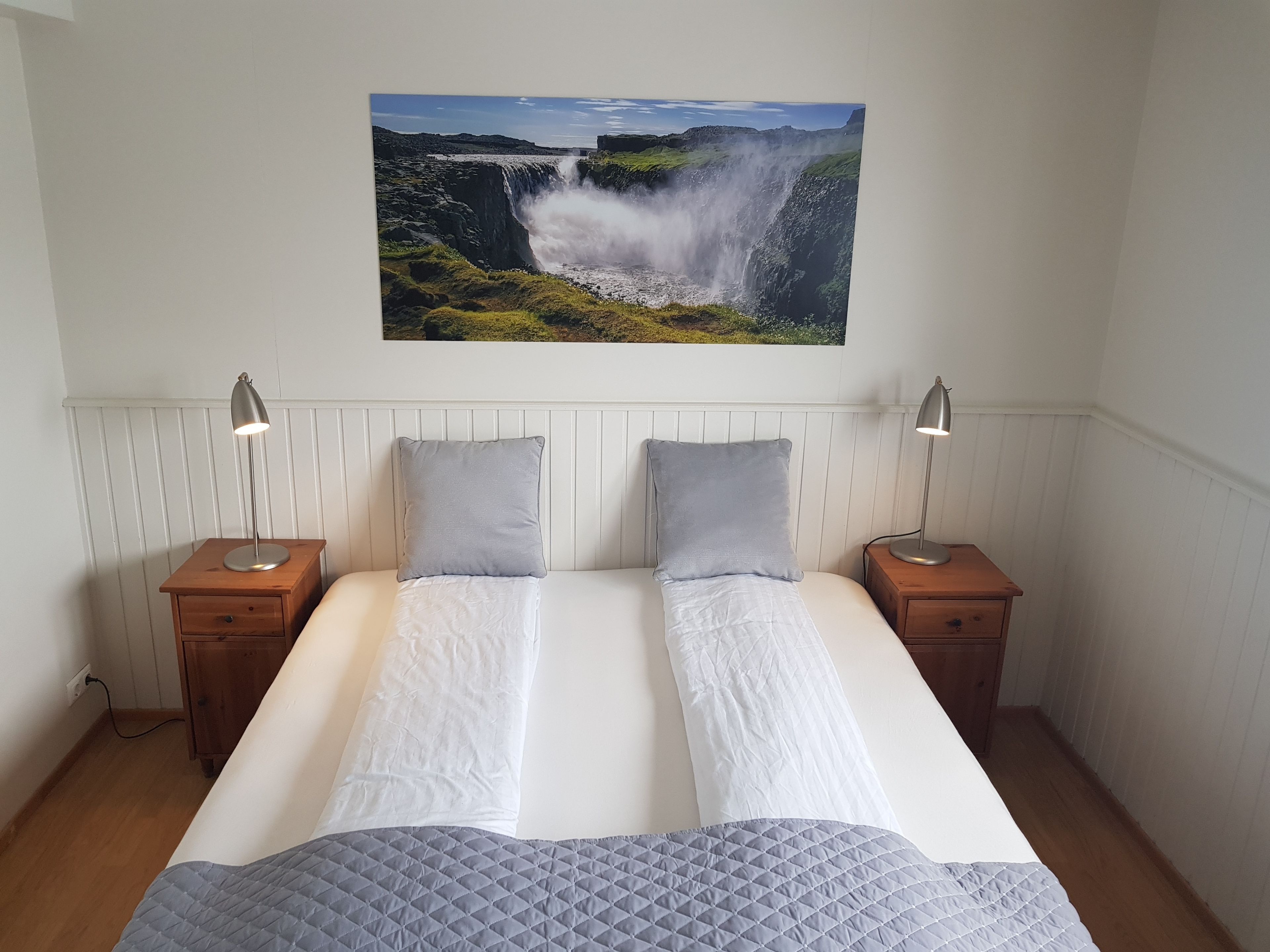 A double bed with two pillows, a quilted blanket, and a wall-mounted picture of a waterfall.