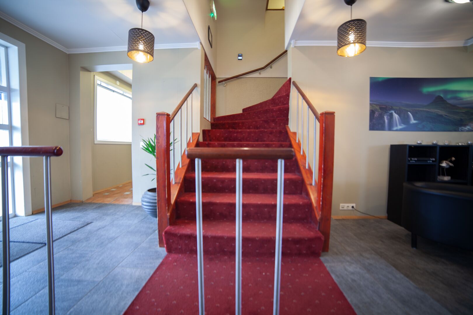 A staircase with red carpet leading to a higher floor, metal railings, and pendant lighting.