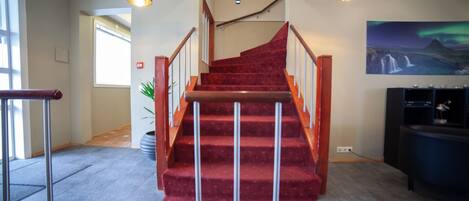 A staircase with red carpet leading to a higher floor, metal railings, and pendant lighting.