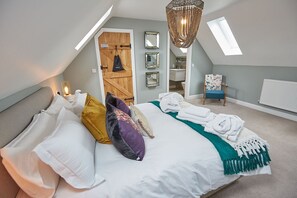 A bedroom with a bed, pillows, a hanging light fixture, a chair, and a door leading to a bathroom. - Wild Cherry Barn (Lincoln)