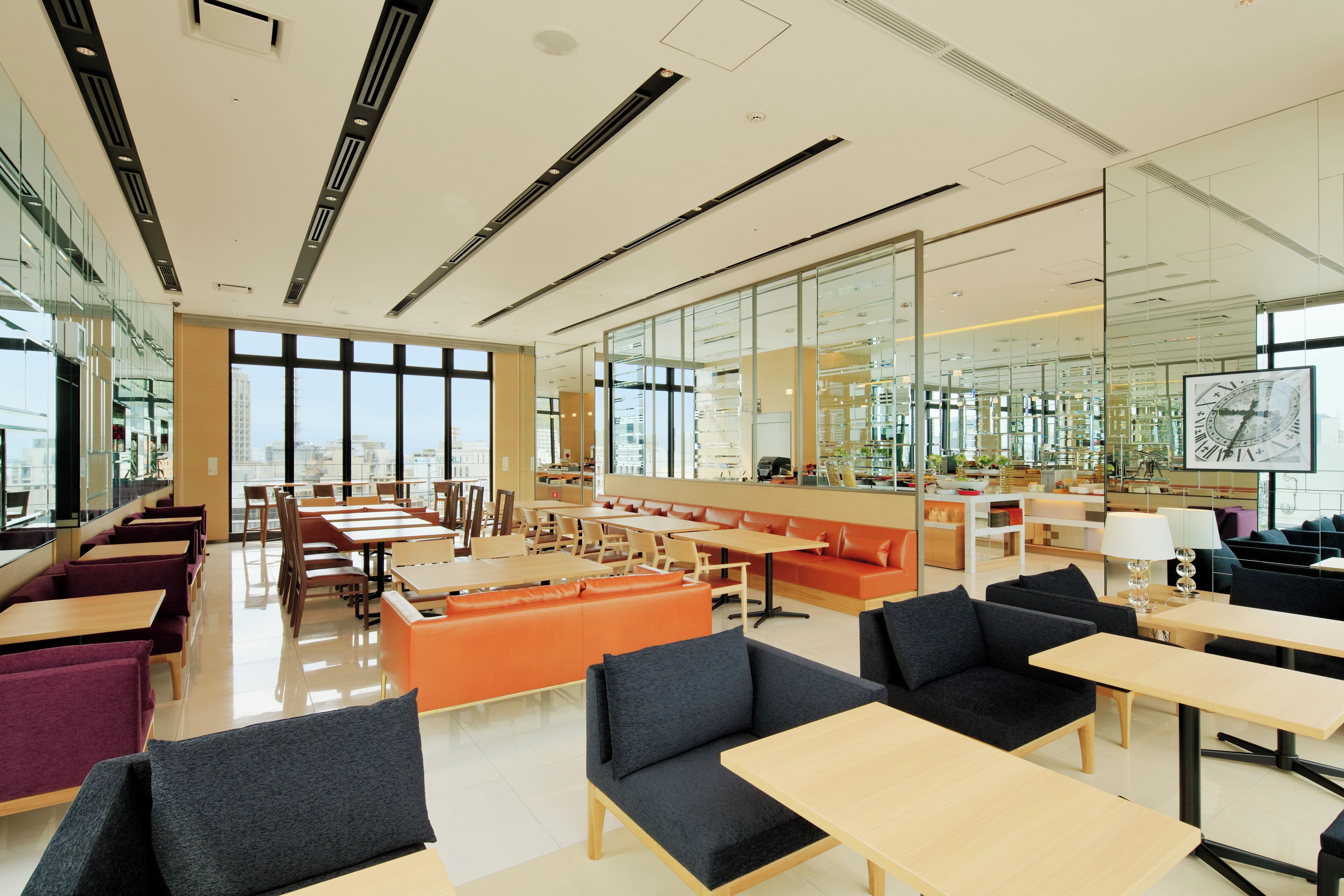 A modern library with multiple seating areas, including tables and couches, and large windows offering views of the city.
