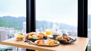 Een ontbijtplateau met diverse soorten eten en een glas sinaasappelsap op een tafel bij een raam met uitzicht over de stad.