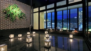 Een moderne lobby met een bakstenen muur, grote ramen en decoratieve verlichting.
