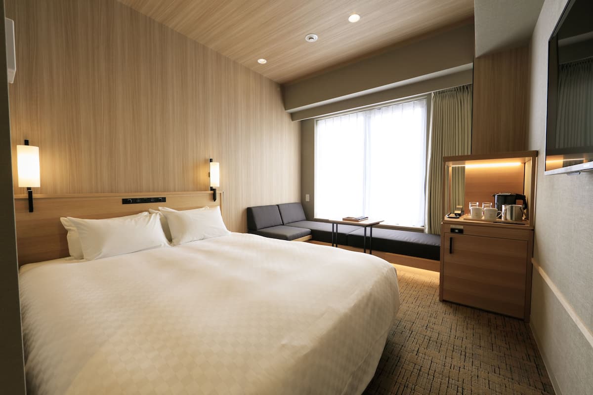 A hotel room with a large bed, a sofa, a desk, and a mirror.