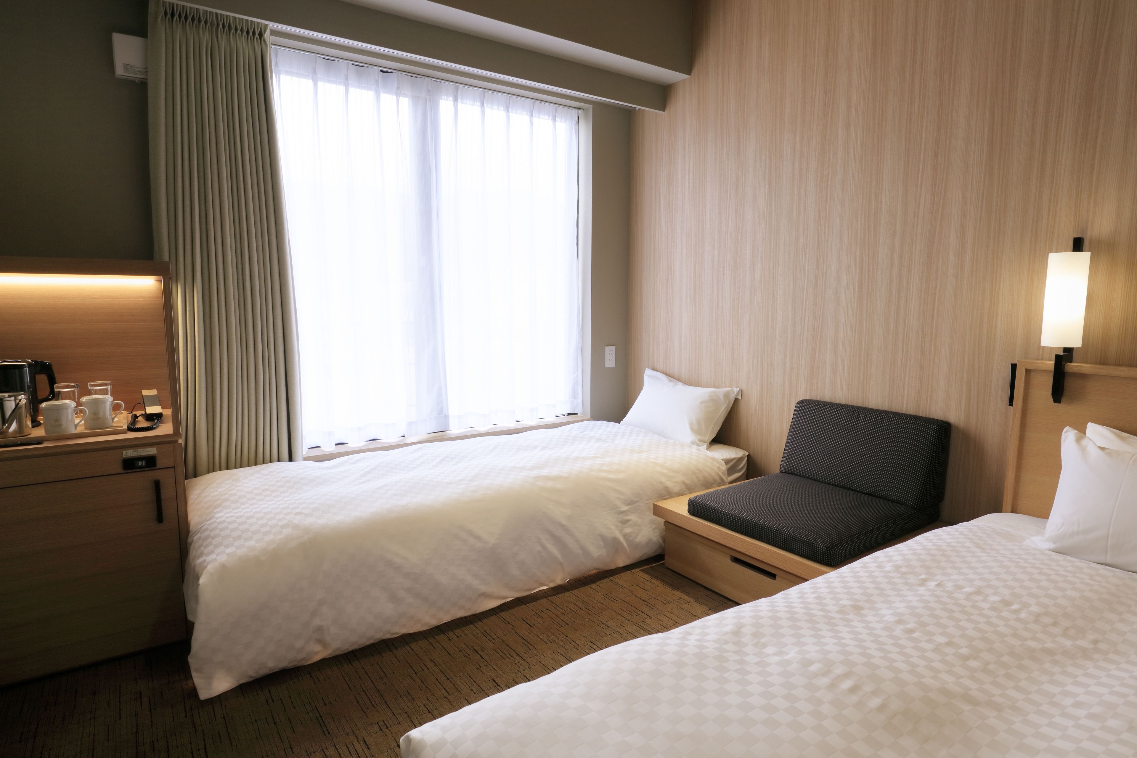 A hotel room with two beds, a desk with a lamp, and a window with curtains.