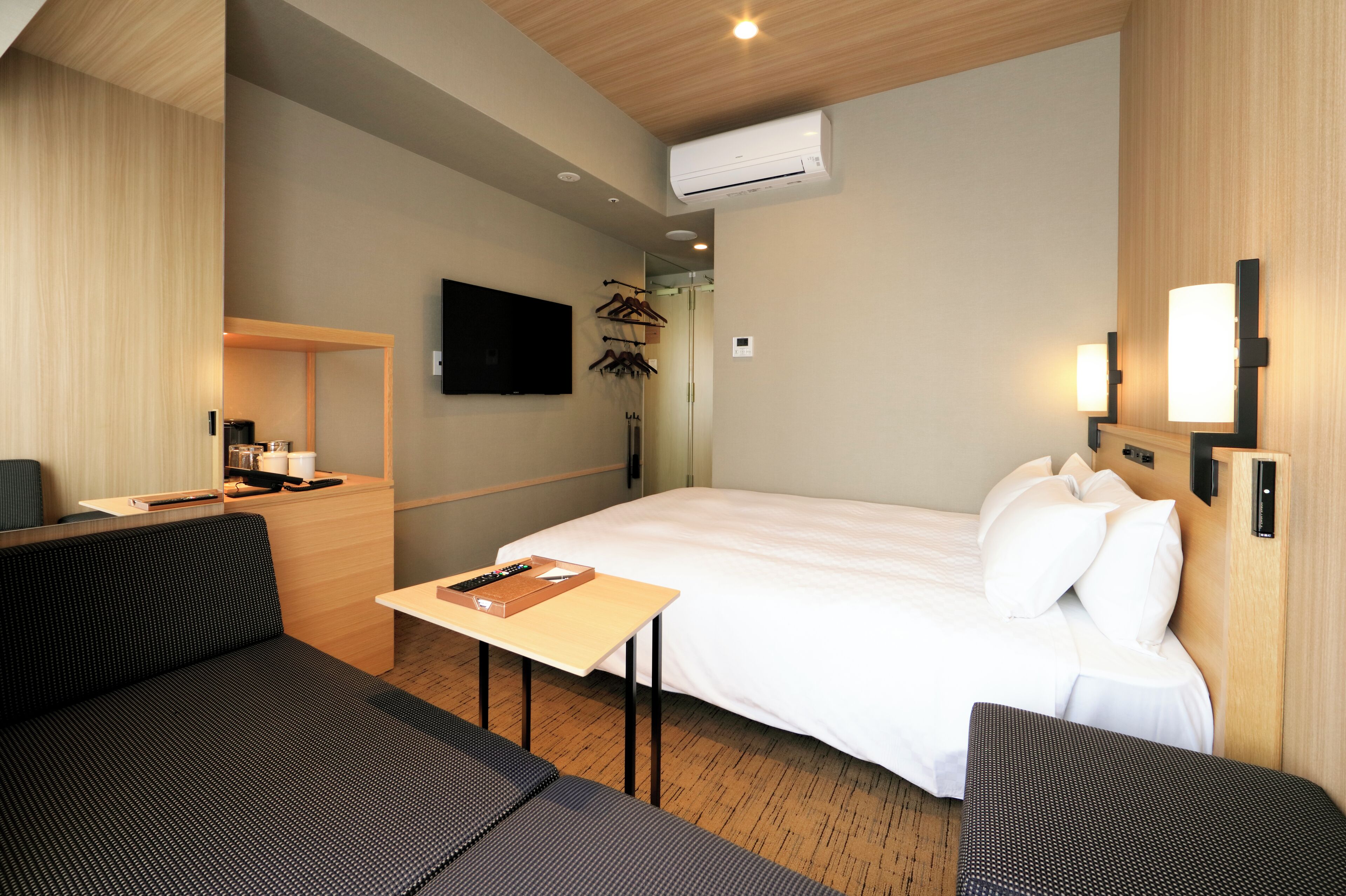 A hotel room with a bed, a desk, a sofa, and a TV mounted on the wall.