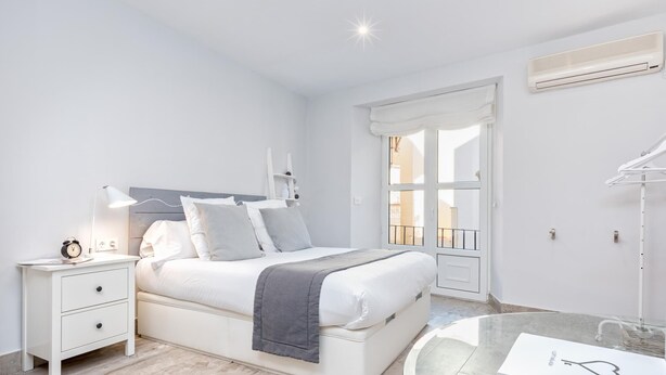 Un dormitorio moderno con cama, mesita de noche, lámpara y una mesa de vidrio con un objeto con forma de corazón.