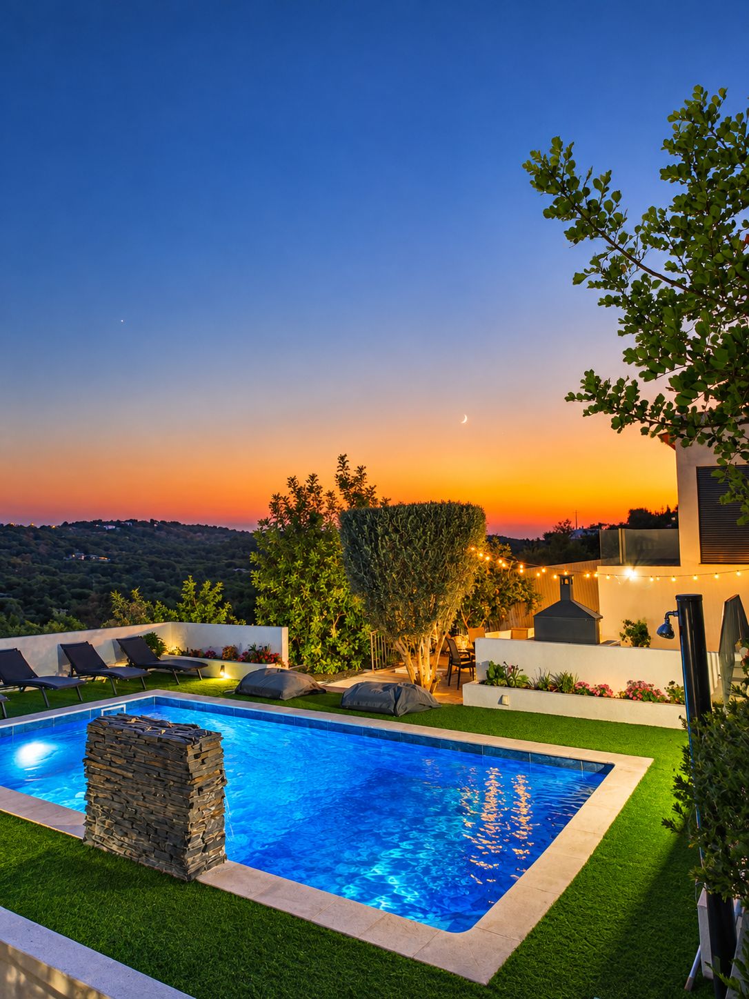 A swimming pool with a stone structure, surrounded by grass and a view of the sunset.