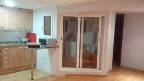 Una cocina con gabinetes de madera, un lavamanos y un microondas. Hay una puerta corrediza de vidrio que da a un balcón con vistas al exterior.