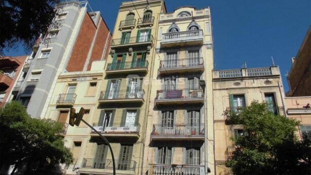 Un edificio de varios pisos con balcones, cielo despejado y árboles.