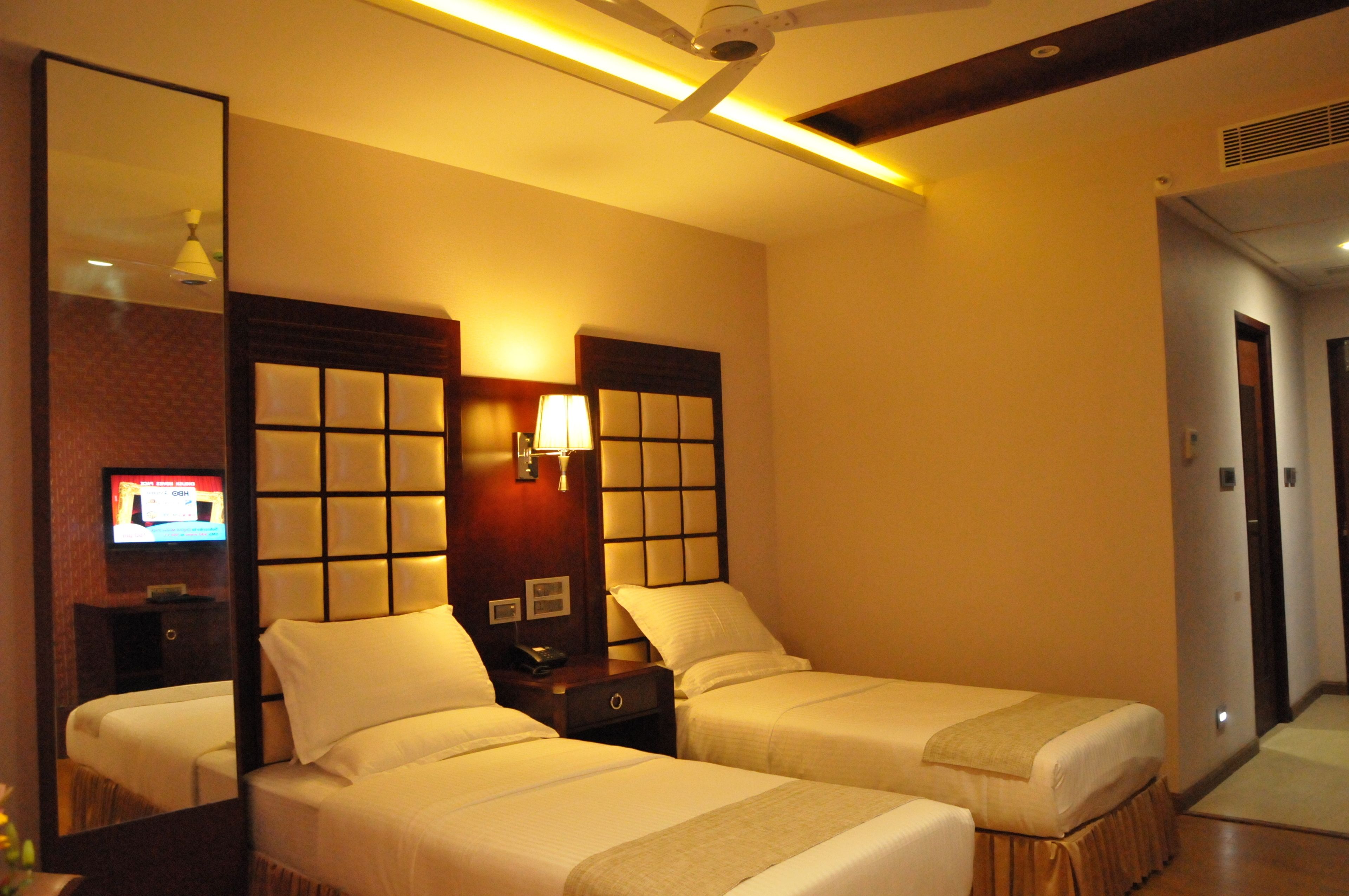 A hotel room with two single beds, a large mirror, a television, and a ceiling fan.