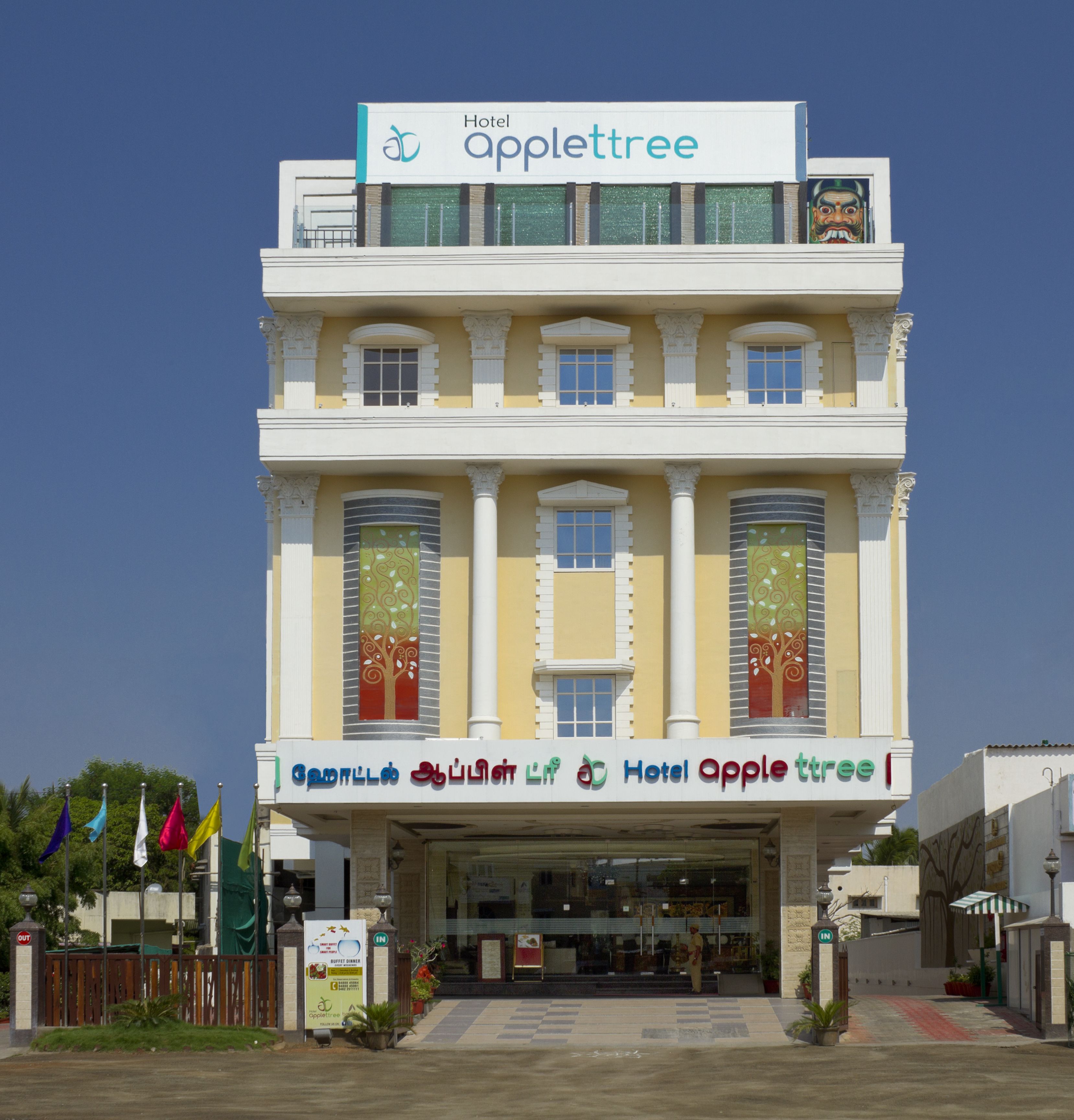 Een hotel genaamd 'Hotel Apple Tree' met een traditionele architectuur, een centrale ingang, meerdere ramen en decoratieve details.