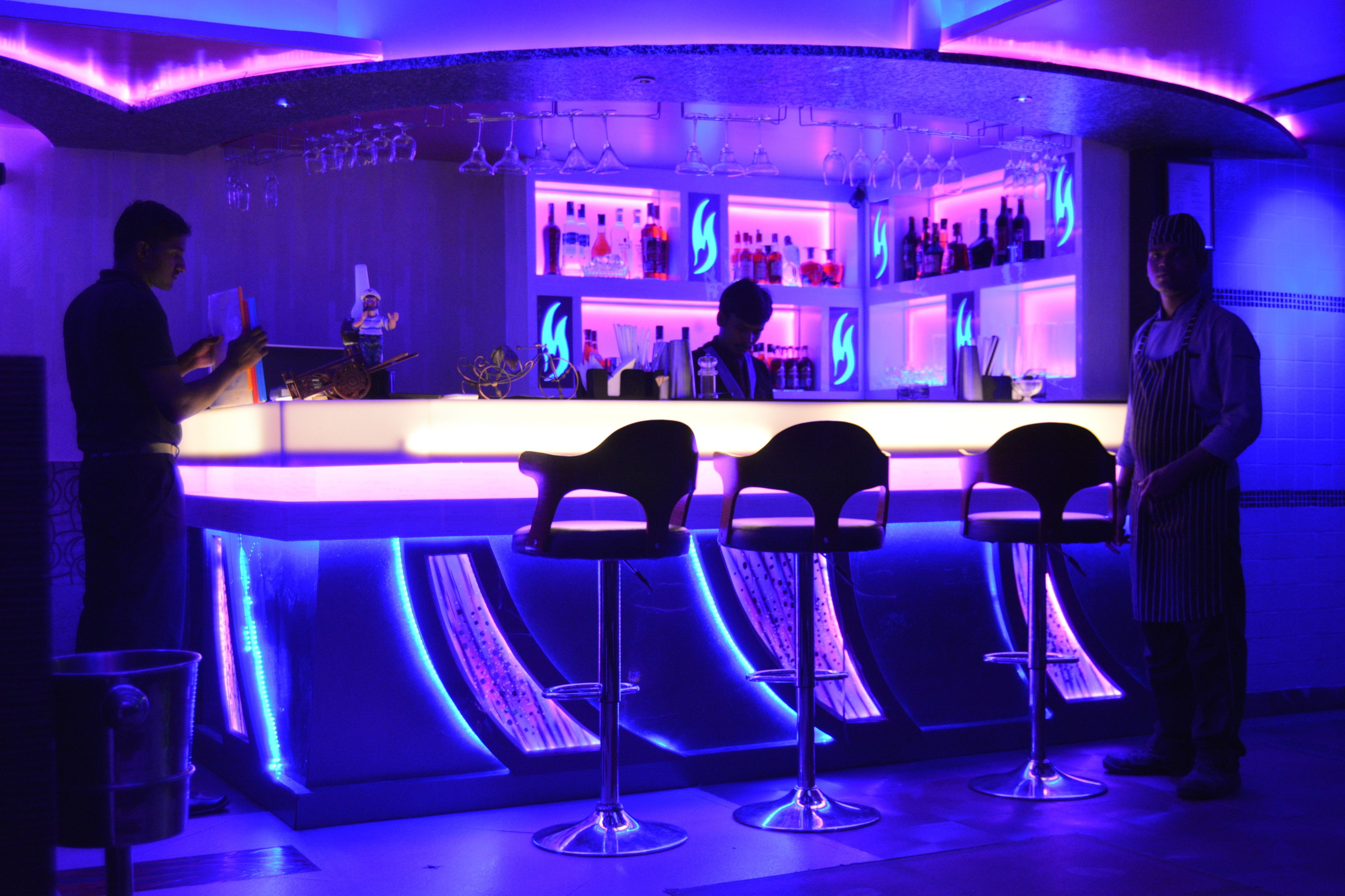 A bar area with a counter, bar stools, and shelves with bottles.