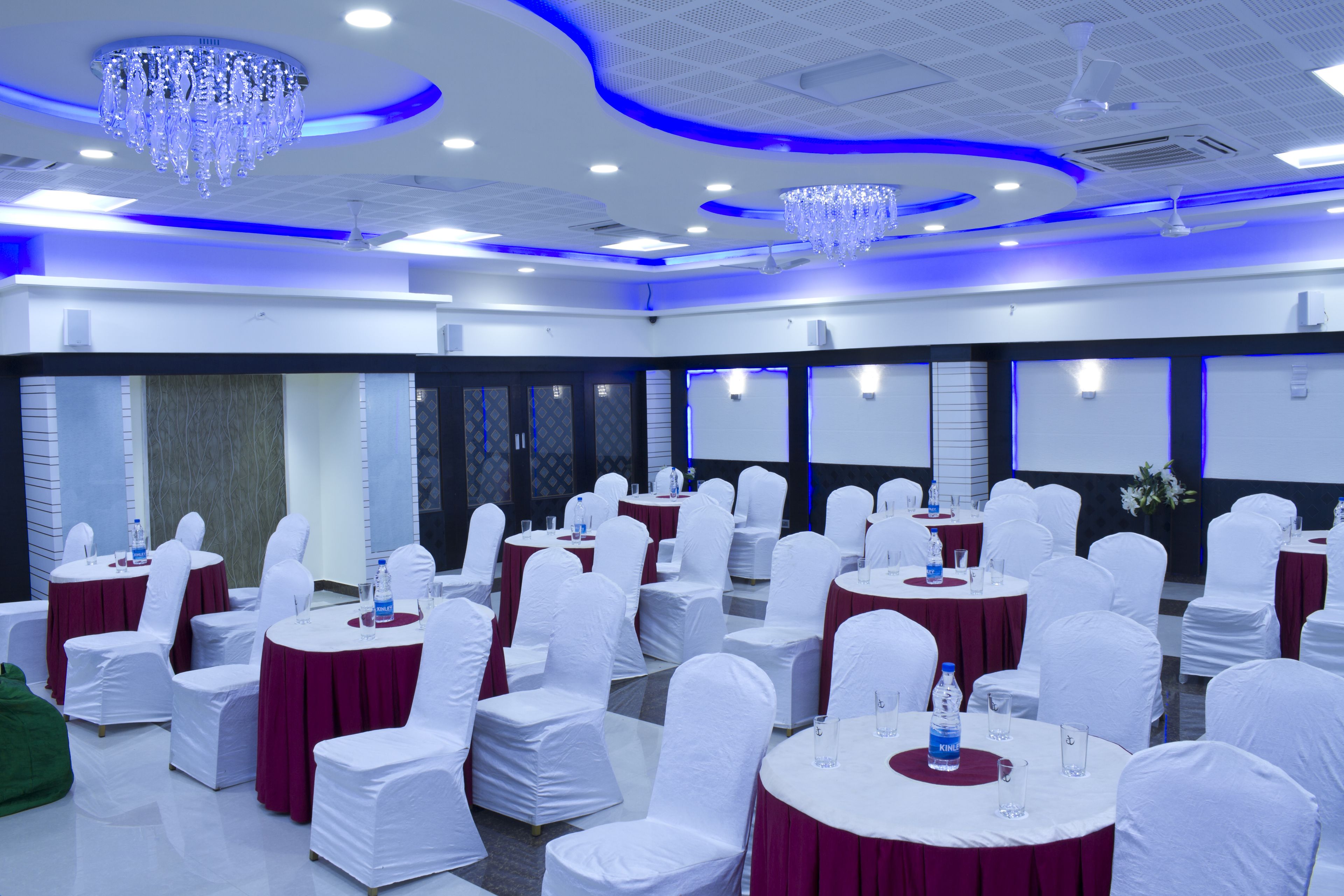 A banquet hall with round tables, white chairs, and blue ambient lighting.