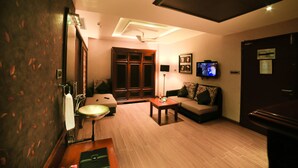 Habitación de hotel con piso de madera, un sofá, una mesa pequeña, un televisor y una puerta.