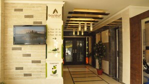 Un vestíbulo de hotel con pared de ladrillo, una televisión montada, señalización direccional para los pisos y una planta en maceta.