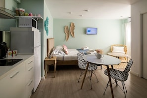 A compact hotel room with a bed, a small table with chairs, a kitchenette, and a TV mounted on the wall.