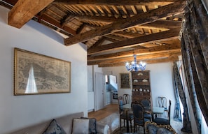 Un espace repas avec des poutres en bois, un lustre, une table à manger, des chaises et, au fond, une cuisine.
