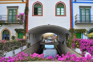Ein Kanal mit einer Brücke, die zwei Gebäude verbindet, beide mit einem Balkon und grünen Türen.
