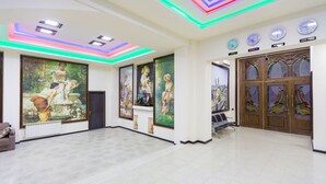 A spacious lobby with a large mural, a reception desk, and a clock displaying time in various cities. - Renessans Hotel Baku (Baku)