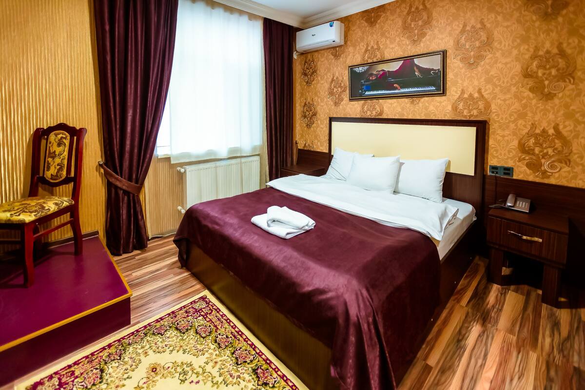 Une chambre d’hôtel avec un lit, une chaise, un bureau et une fenêtre avec des rideaux.