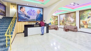 A reception area with a reception desk, a staircase with yellow railings, and a large mural on the wall. - Renessans Hotel Baku (Baku)