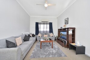 A living room with a grey sofa, a coffee table, a TV stand, and a ceiling fan. - Discover Cessnock Vineyard Delights - Book Direct (Cessnock)