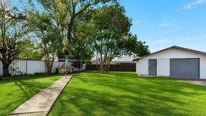 Une cour bien entretenue, recouverte de gazon, avec un chemin en béton menant à un bâtiment doté d’un garage.