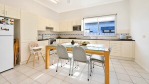 Une cuisine moderne avec un coin repas, des meubles blancs, un ventilateur de plafond et une fenêtre avec des stores.