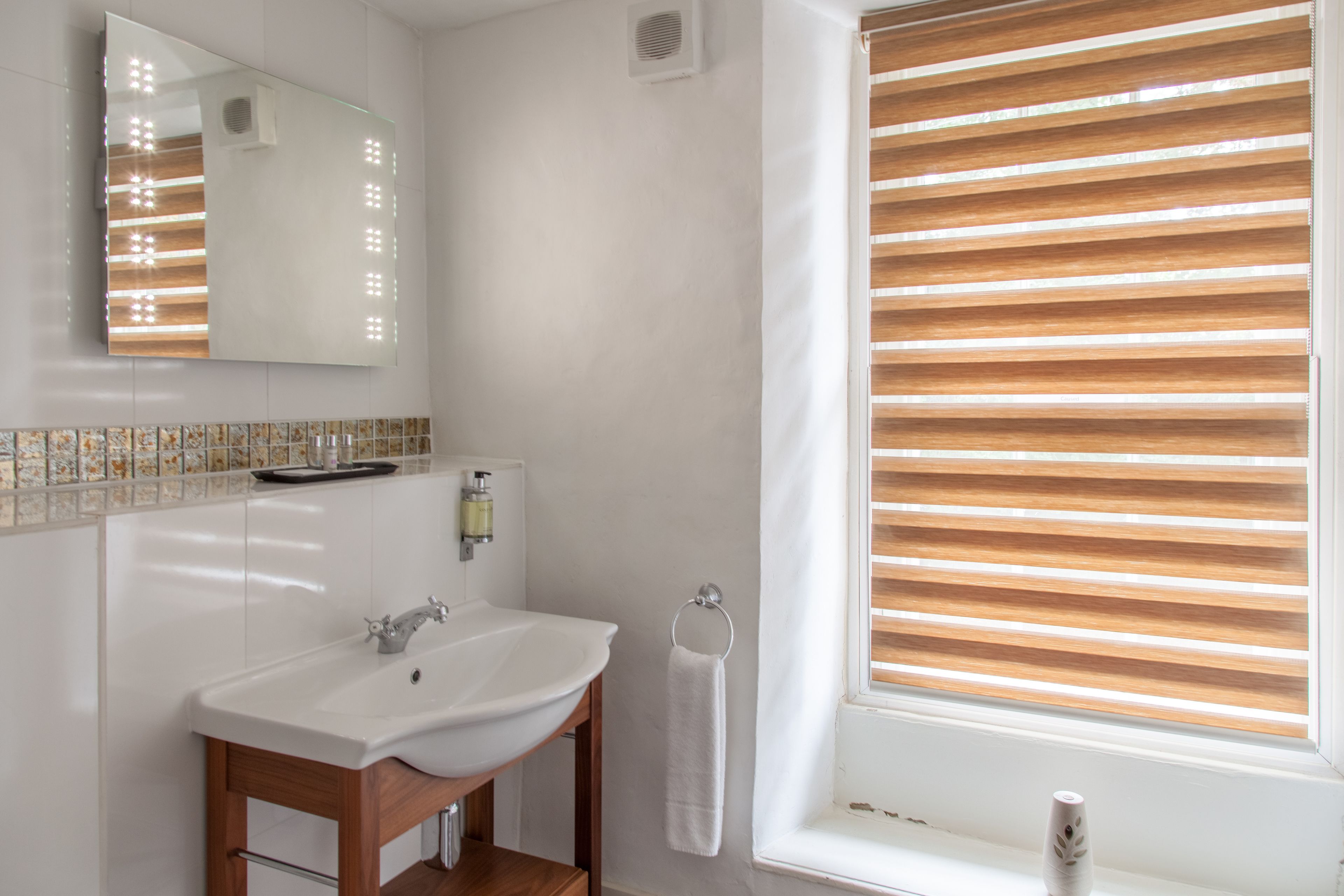 A bathroom with a white sink, mirror, and window with blinds.