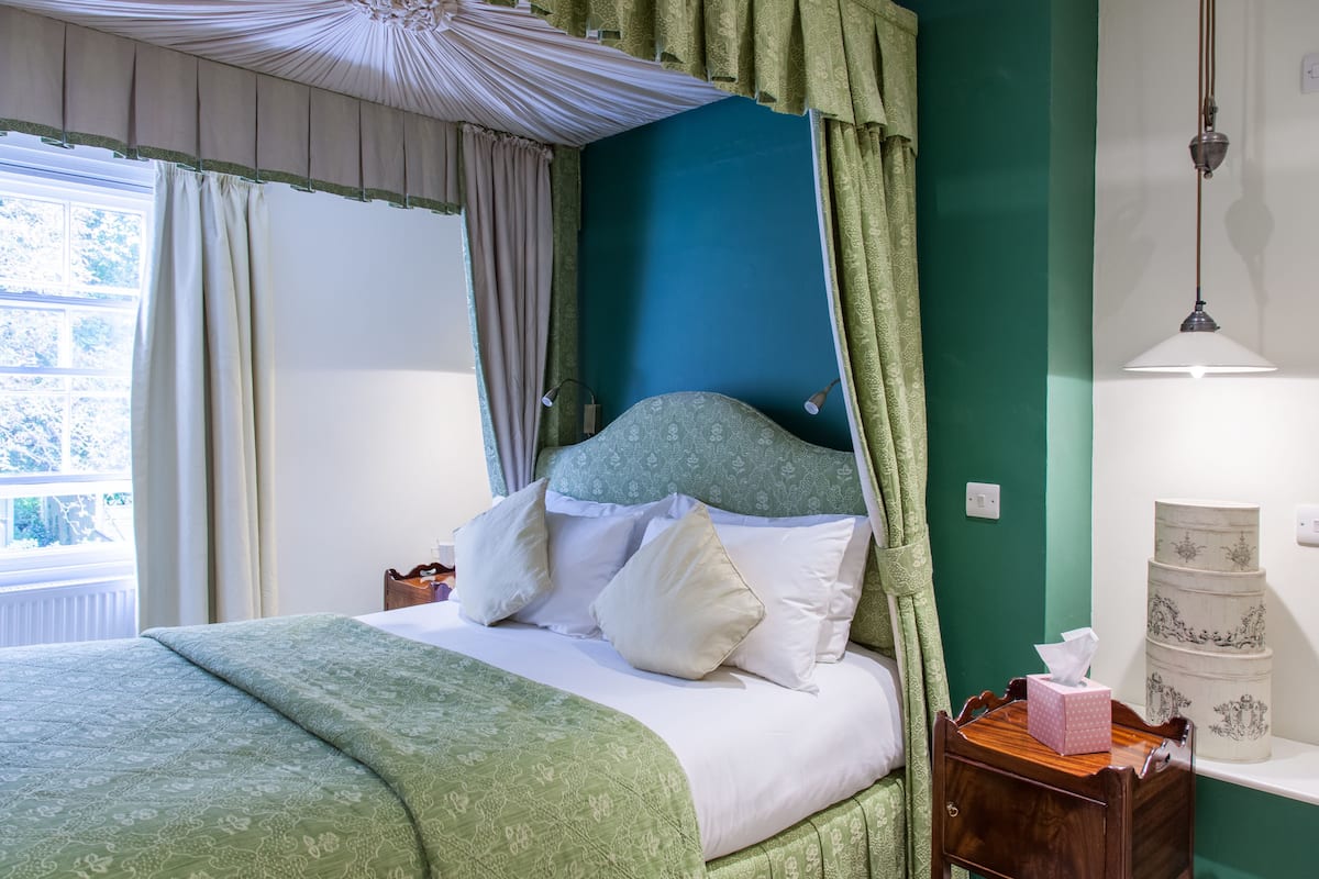 A neatly made bed with a green bedspread, a wooden nightstand with a tissue box, and a green wall.