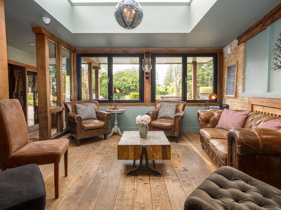 Une pièce meublée de meubles en cuir, avec une table basse en bois et de grandes fenêtres donnant sur un paysage verdoyant.