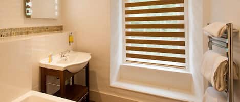 Un bagno con un lavandino bianco, uno specchio e una finestra con persiane.