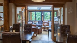 A spacious room with a high ceiling, wooden beams, and large windows offering a view of greenery outside.