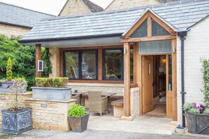 A building with a covered patio area, stone walls, and wooden doors. - The Wychwood Inn (Chipping Norton)