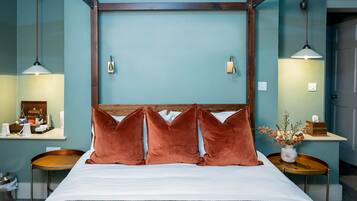 Quarto de hotel com cama, duas mesas de cabeceira, um criado-mudo, luminária na parede e um vaso com flores.