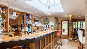 A bar area with a wooden counter, bar stools, and a variety of bottles and glasses.