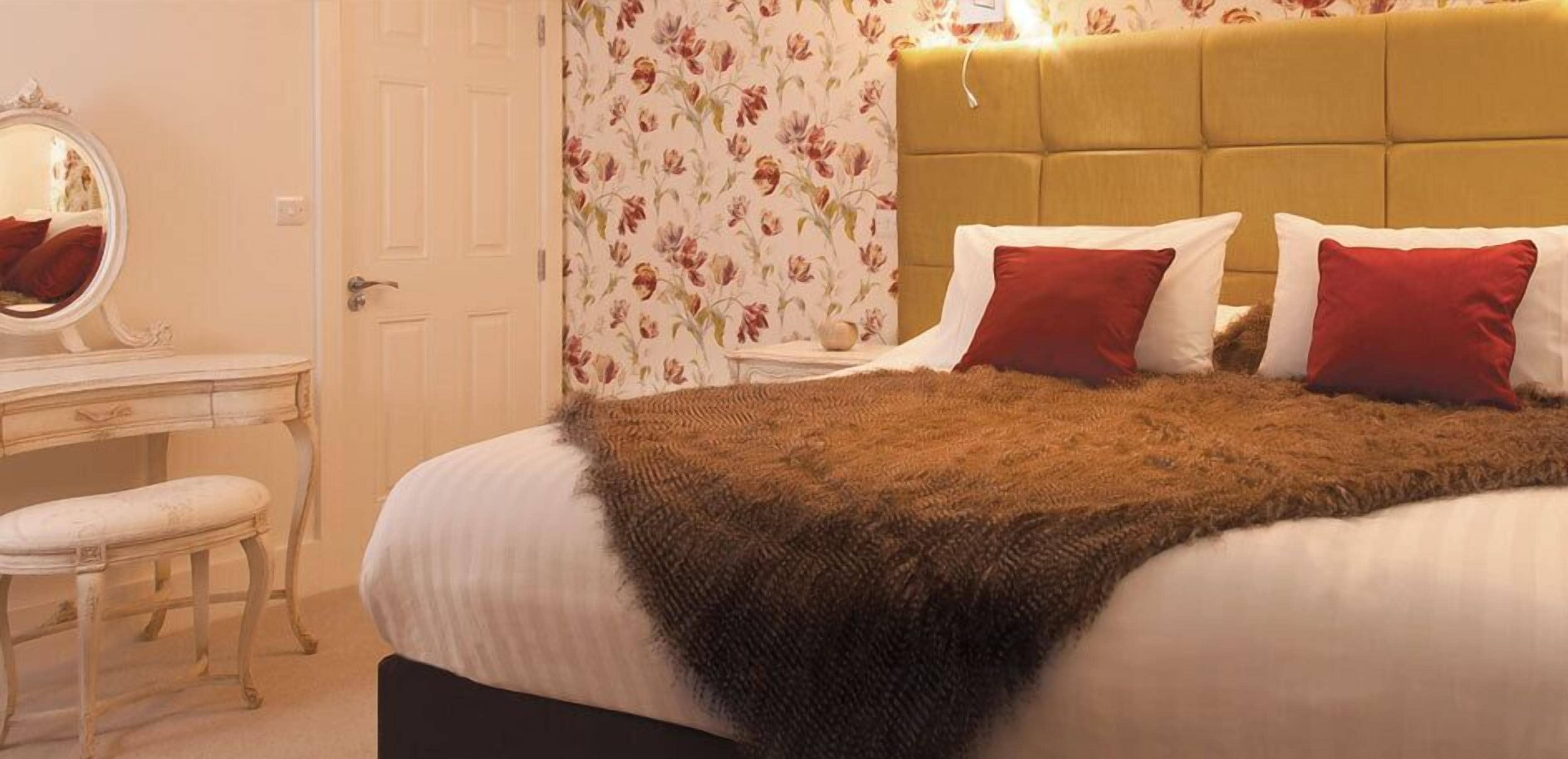 A bedroom with a bed, a bedside table, a mirror, and a floral wallpaper.