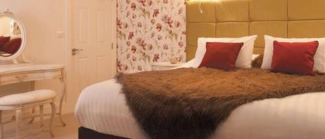 A bedroom with a bed, a bedside table, a mirror, and a floral wallpaper.