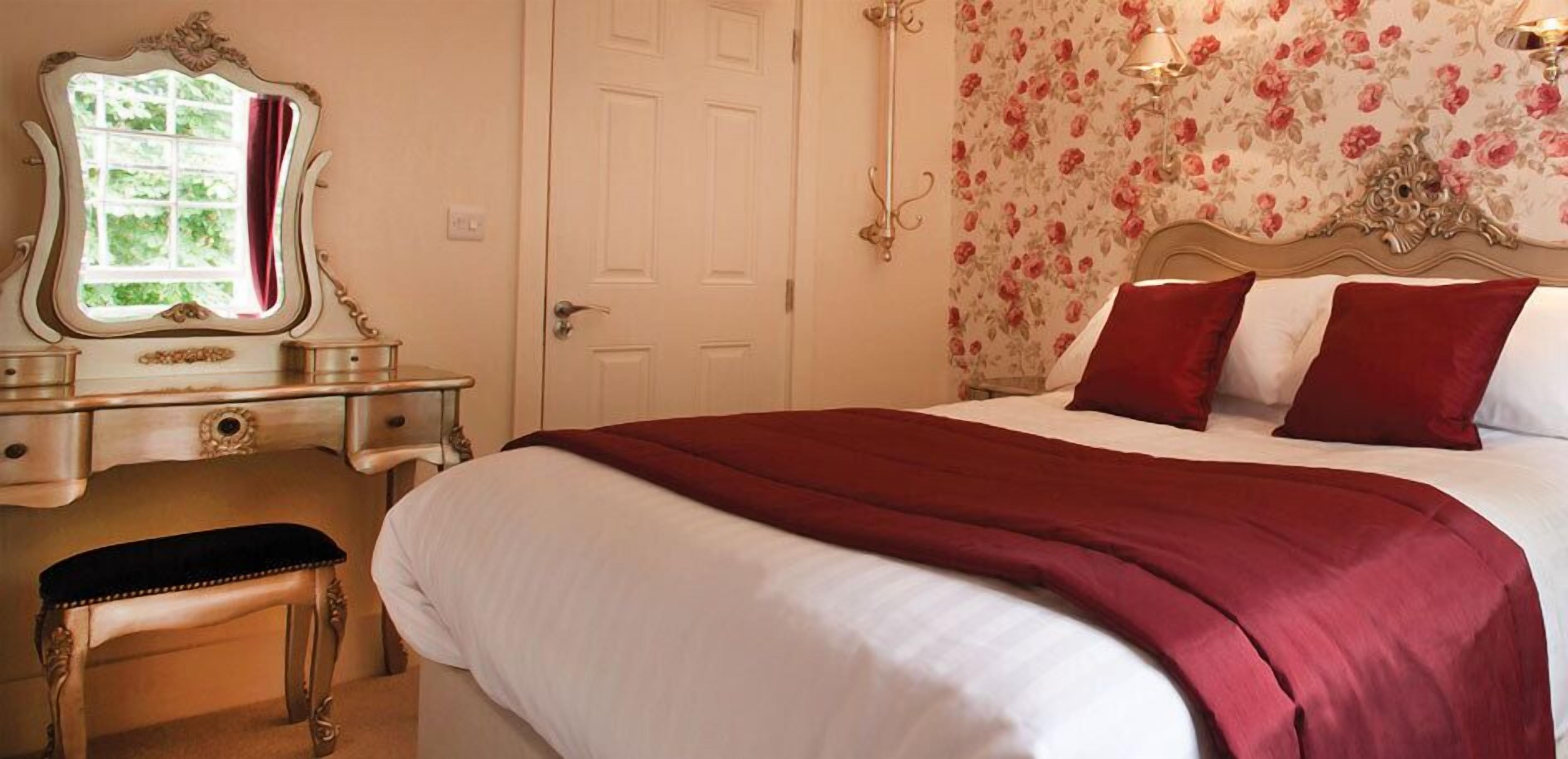 A bedroom with a large bed, a vanity with a mirror, a door, and floral wallpaper.