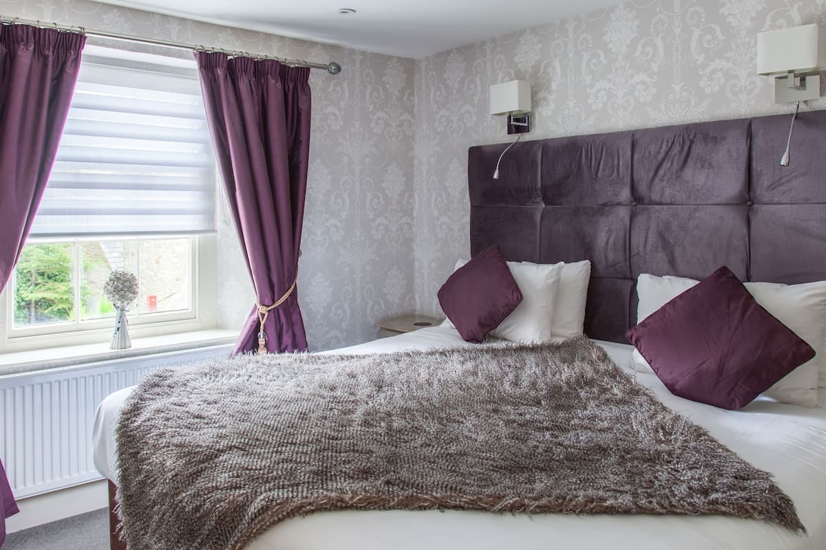 A bedroom with a large bed, a headboard, and a window with curtains.