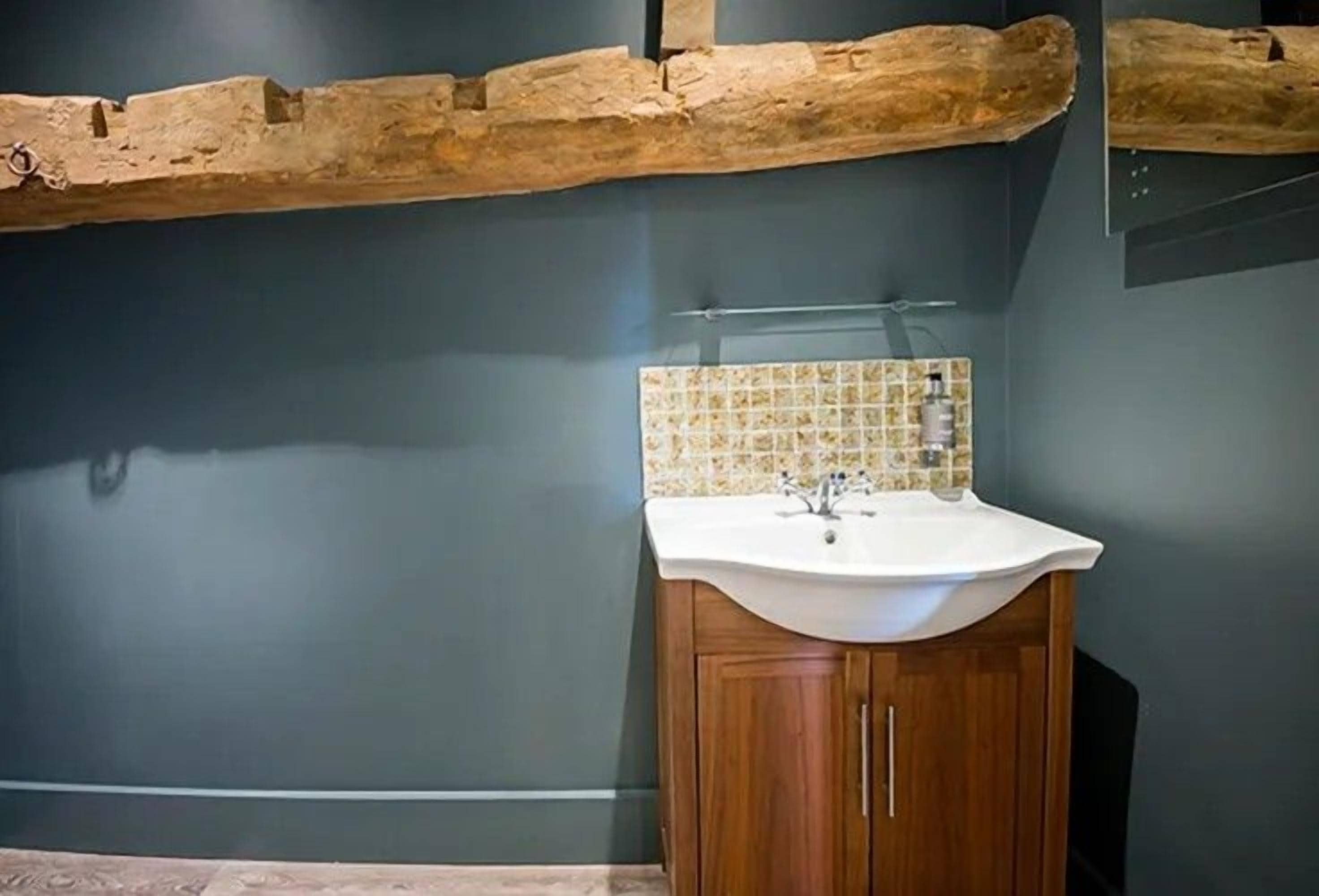 A bathroom with a wooden cabinet, a white sink, and a tiled backsplash.