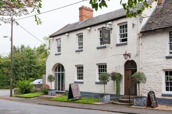 A traditional white building with a signboard, arched windows, and a door. - The Wychwood Inn (Chipping Norton)