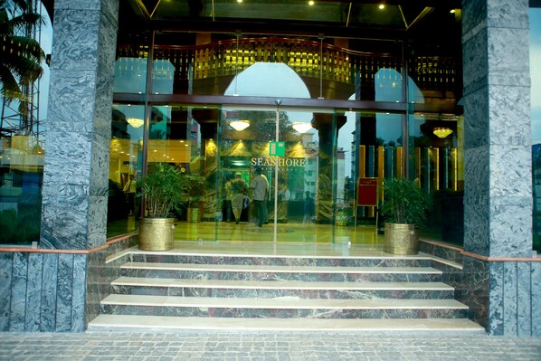 L’entrée d’un hôtel, avec des marches en marbre, des portes en verre et des plantes en pot.