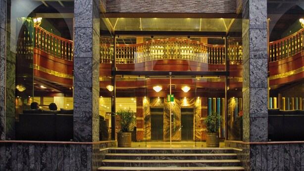 L’entrée d’un hôtel, avec une façade en marbre, une porte vitrée et un balcon doté de balustrades.