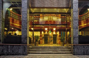 L’entrée d’un hôtel, avec une façade en marbre, une porte vitrée et un balcon doté de balustrades.