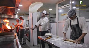 Una cocina comercial con cocineros preparando alimentos, un letrero que indica una carnicería y el logotipo de Seashore Residency.