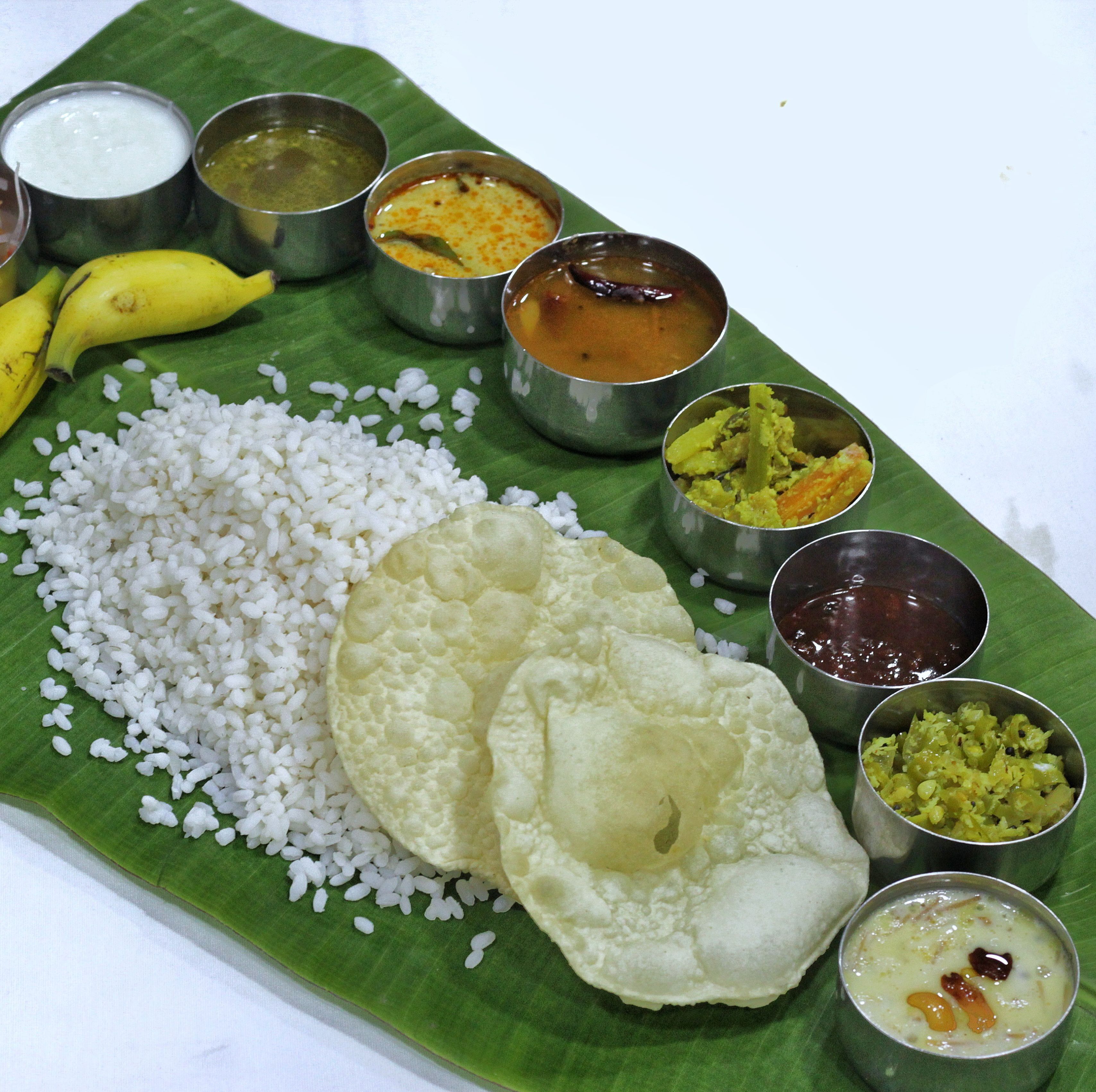 A traditional South Indian meal served on a banana leaf with rice, two dosas, and various accompaniments in metal bowls.