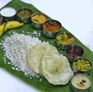 A traditional South Indian meal served on a banana leaf with rice, two dosas, and various accompaniments in metal bowls. - Seashore Residency (Kodungallur)
