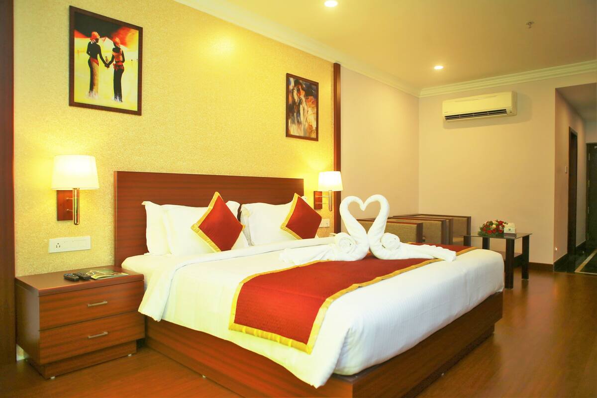A hotel room with a large bed, two bedside tables, a nightstand, and wall-mounted air conditioning.